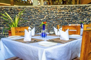 Una mesa para cuatro con manteles blancos, jarrones azules y un fondo de pared de piedra.