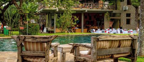 A poolside area with wooden furniture and a building with a thatched roof in the background.