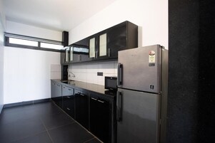 Una cocina moderna con armarios negros, un refrigerador de acero inoxidable y un microondas empotrado.