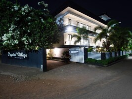 Un edificio de varios pisos con entrada protegida por una reja, rodeado de vegetación y palmeras.
