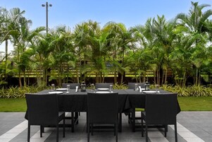 Un área de comedor al aire libre con una mesa dispuesta para cuatro personas, rodeada de abundante vegetación y palmeras.