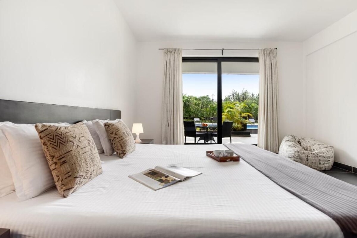 A hotel room with a large bed, a view of the outdoors, and a dining area.