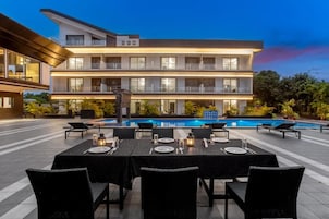 Un hotel de varios pisos con piscina, zona de comedor al aire libre y una fachada bien iluminada.