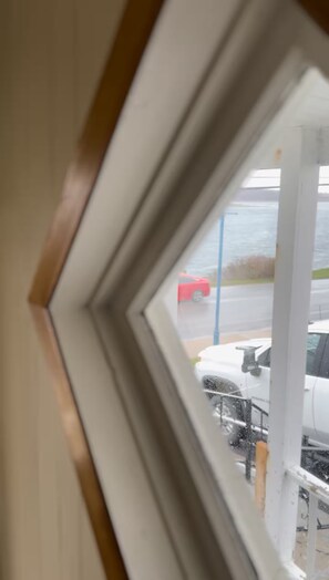 Blick durch ein Fenster mit weißem Rahmen auf einen Parkplatz, auf dem ein rotes Auto und ein weißes Fahrzeug stehen.