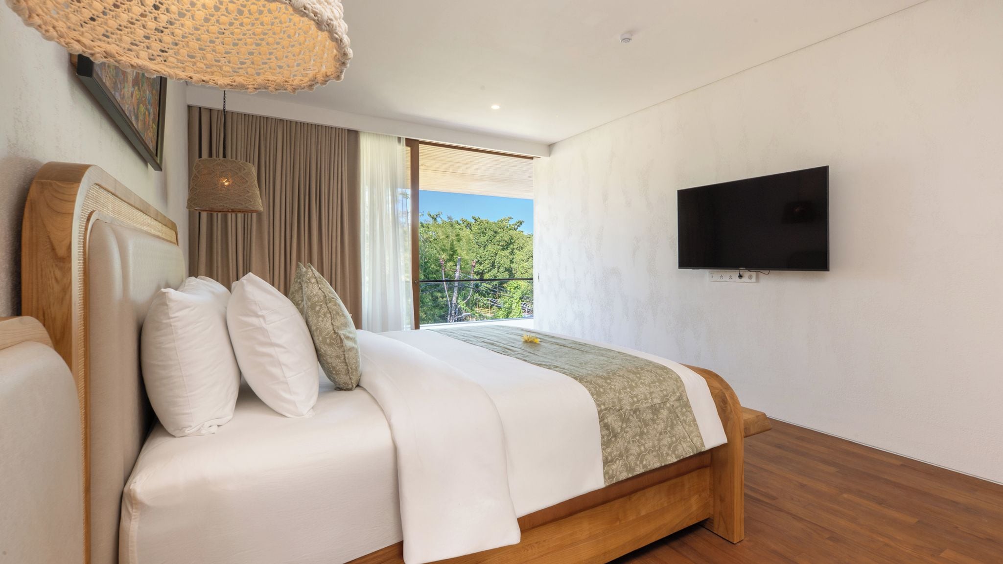 A modern bedroom with a wooden bed, a television on the wall, and a view of greenery outside.