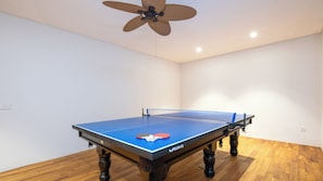 A ping pong table with a ceiling fan in a room with wooden flooring and white walls. - The Atma Bali (Denpasar)
