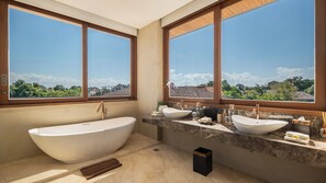 A modern bathroom with a freestanding bathtub, two sinks, and large windows offering a view of the cityscape. - The Atma Bali (Denpasar)