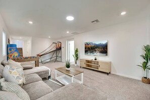 A living room with a sofa, coffee table, TV stand, and a foosball table. - 2700SF Modern 5B3B｜Near Strip｜TVs in all Rooms (Las Vegas)