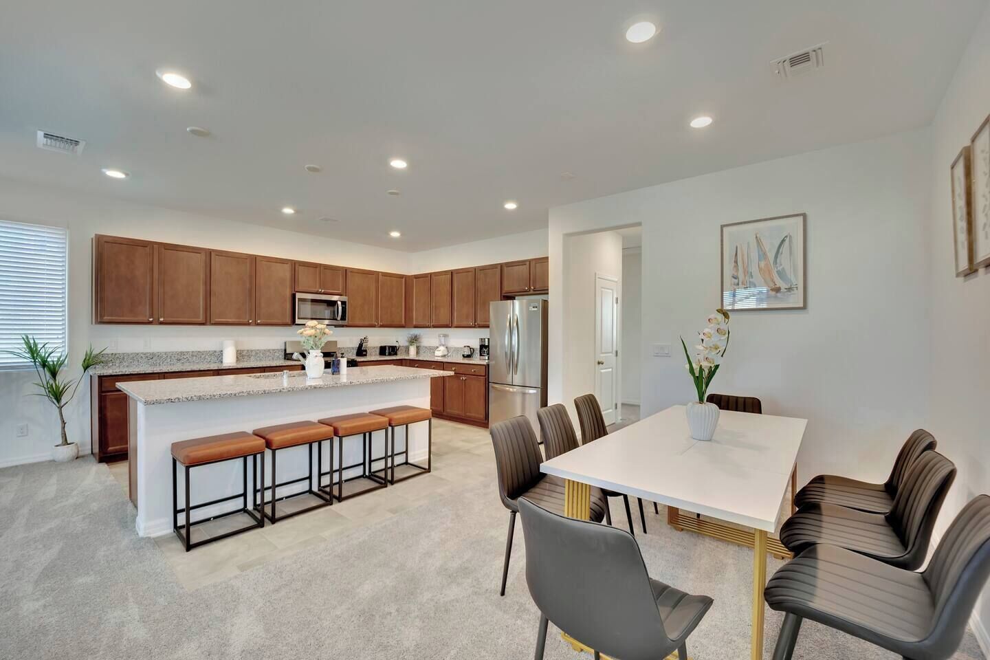 A modern kitchen with wooden cabinets, a central island with bar stools, and a dining area with a white table and chairs.