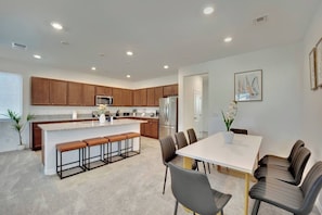 A modern kitchen with wooden cabinets, a central island with bar stools, and a dining area with a white table and chairs. - 2700SF Modern 5B3B｜Near Strip｜TVs in all Rooms (Las Vegas)