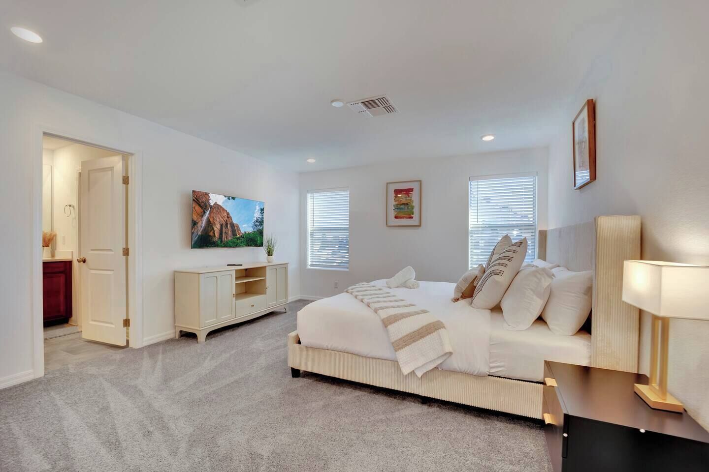 A modern bedroom with a large bed, a bedside table, a TV, and a window with blinds.