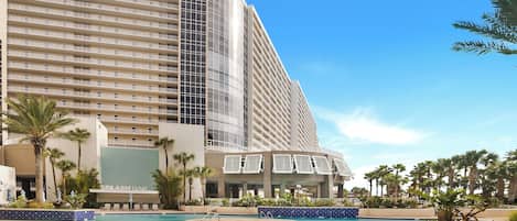 Un hotel con piscina, palmeras y un edificio grande con balcones.