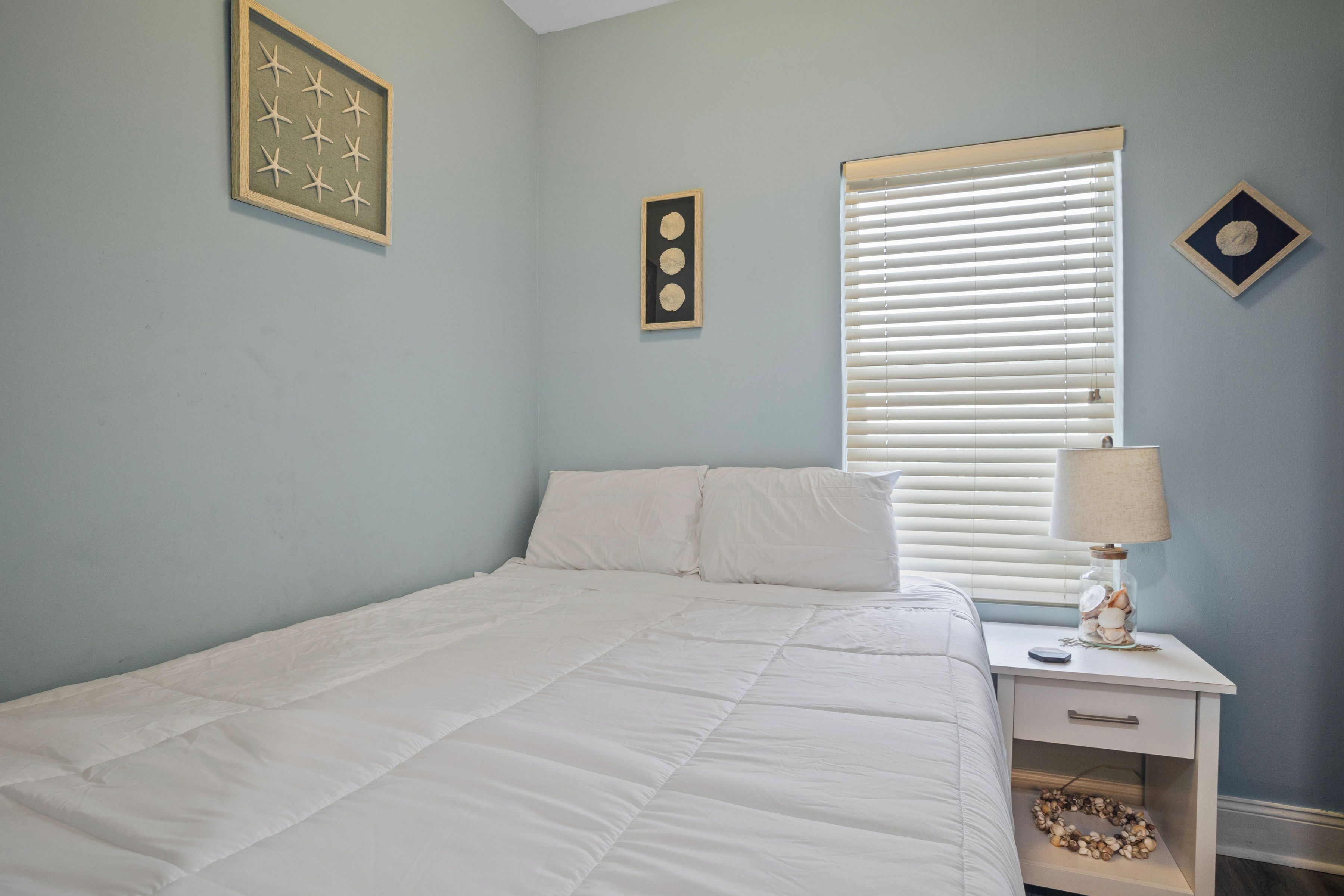 A bedroom with a bed, a nightstand, a lamp, and wall decorations.