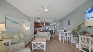 A spacious living area with a sofa, coffee table, and dining table. A kitchen is visible in the background. - Laketown Wharf 824 (Panama City Beach)