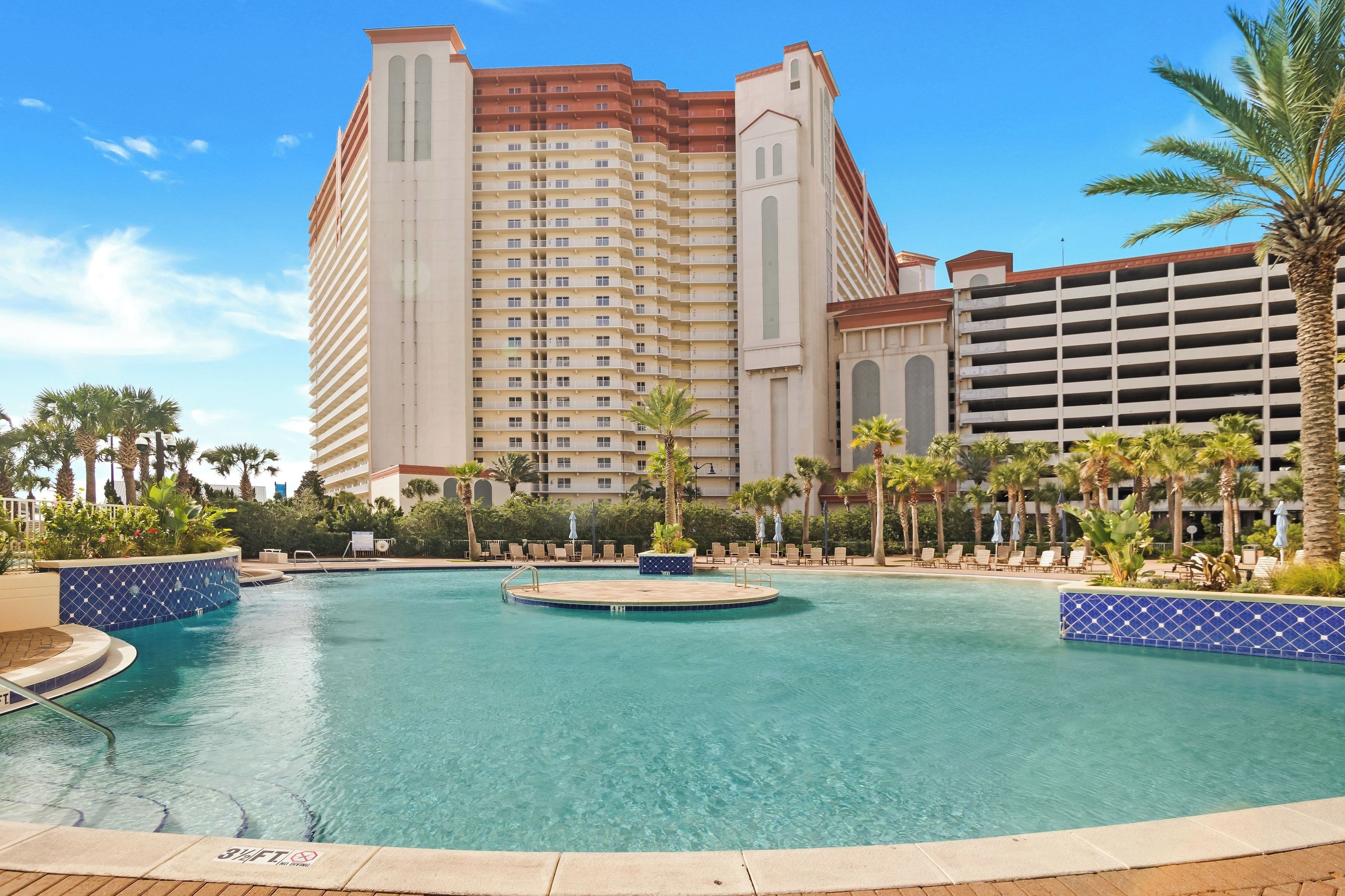A hotel with a large pool, palm trees, and a multi-story building with balconies.