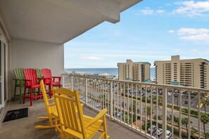 Un balcon donnant sur un parking et des immeubles, agrémenté de chaises Adirondack aux couleurs vives.