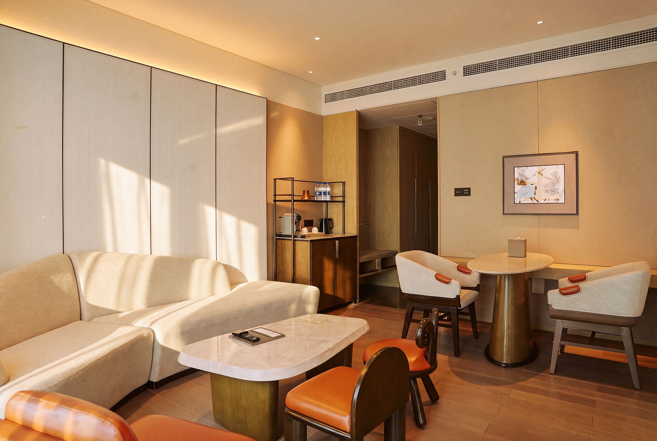 Quarto de hotel moderno com sofá, uma pequena mesa e área de refeições com cadeiras.
