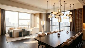 A modern hotel room with a large dining table, sofas, and a city view.