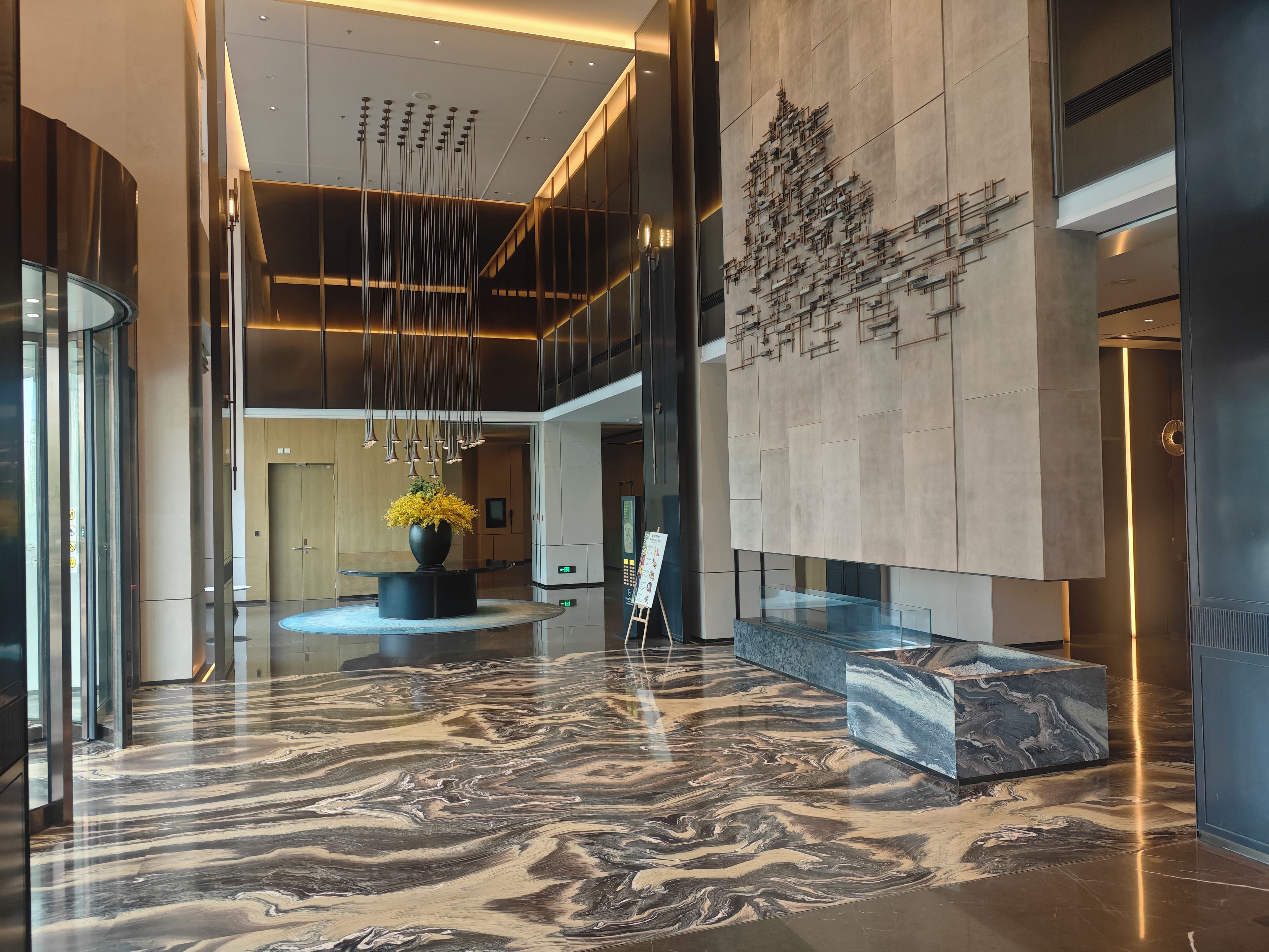 A modern lobby with a marble floor, a central floral arrangement, and a contemporary art piece on the wall.