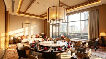 A hotel dining room with a round table set for a meal, surrounded by chairs, with a large window offering a city view.