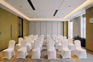 A conference room with rows of white chairs, a clock on the wall, and a carpeted floor.