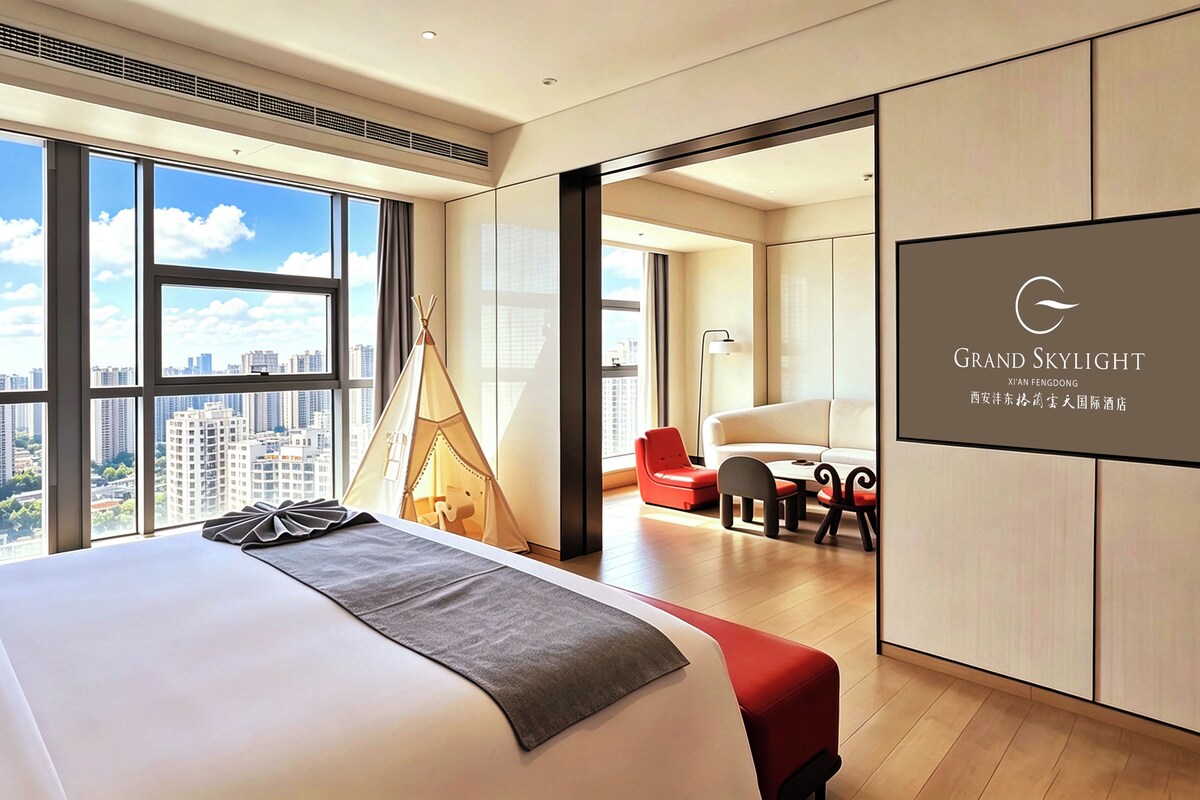 Quarto de hotel moderno com uma cama grande, vista para a cidade, uma cadeira vermelha e um abajur preto.