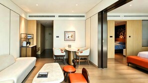 Habitación de hotel moderna con sofá, una mesita, cafetera y cama con detalles color naranja.