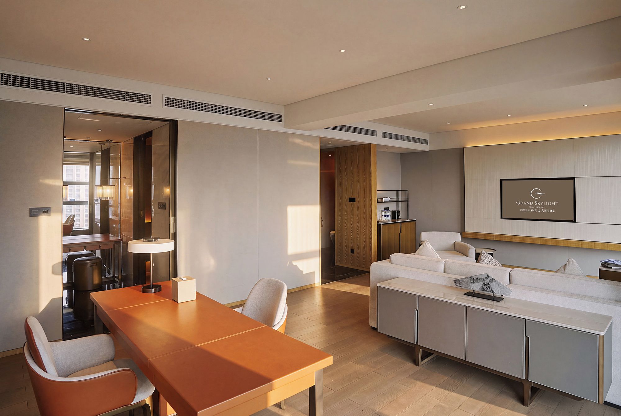 A modern hotel room with a dining area, a sofa, and a television mounted on the wall.