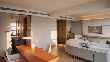 A modern hotel room with a dining area, a sofa, and a television mounted on the wall.