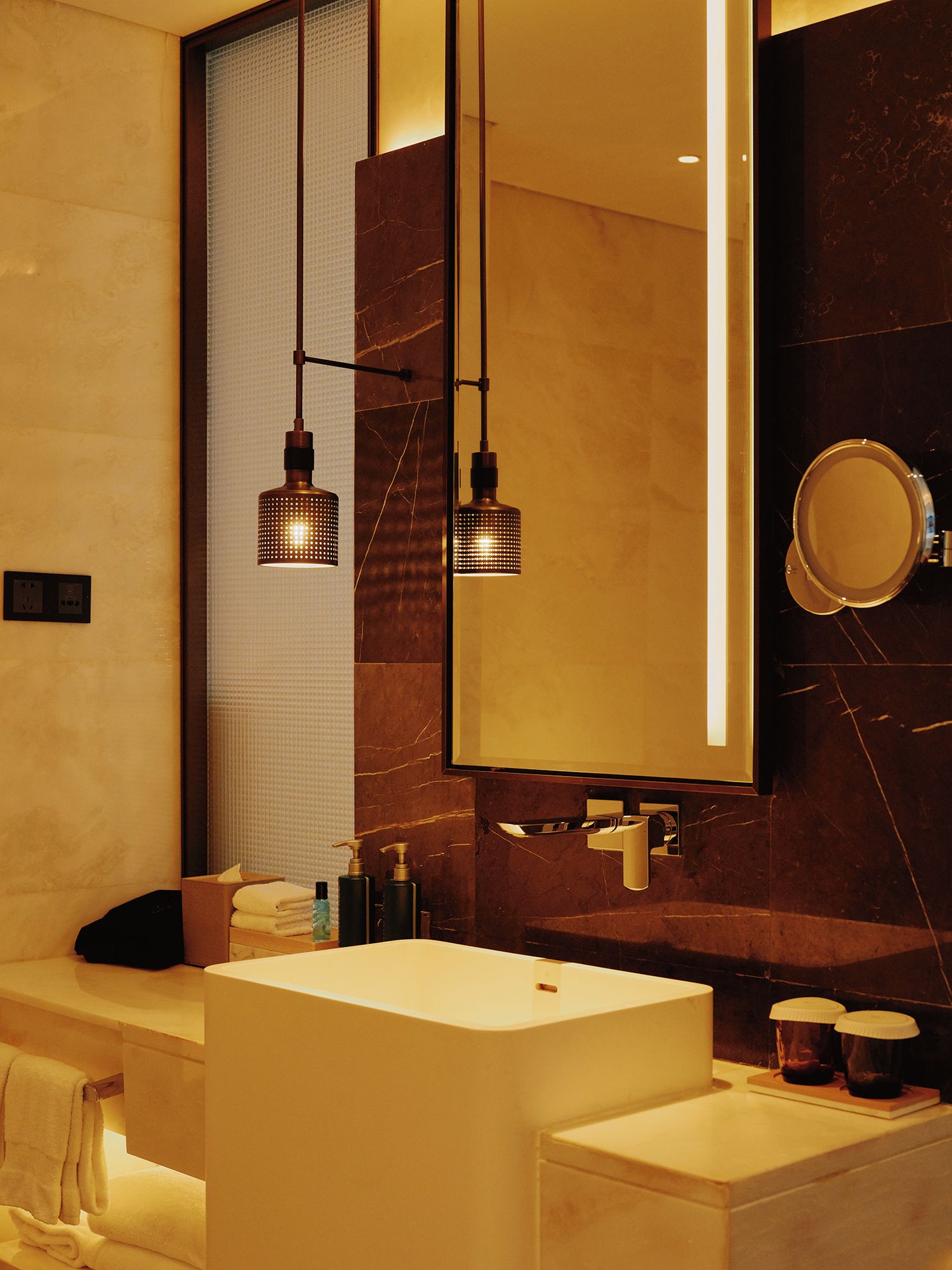 A modern bathroom with a large mirror, two pendant lights, a white sink, and a towel rack.