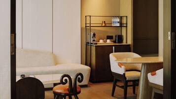 A modern hotel room with a sofa, a dining table, and a small stool.