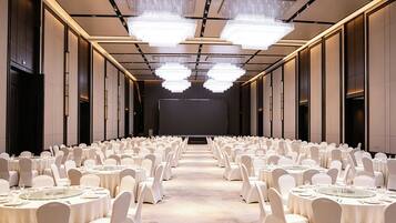 A conference room with rows of round tables, white chairs, and a large screen at the front.