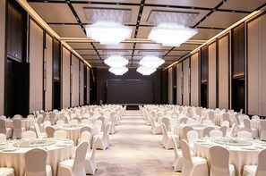 Un salón de conferencias con filas de mesas redondas, sillas blancas y una pantalla grande al frente.