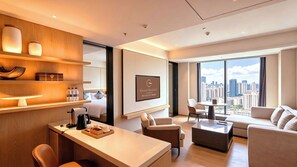 Quarto de hotel moderno com cama, escrivaninha com cafeteira, sofá, poltrona e grande janela com vista para a cidade.