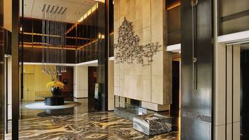 A modern lobby with a marble floor, a central art installation, and a reception desk.