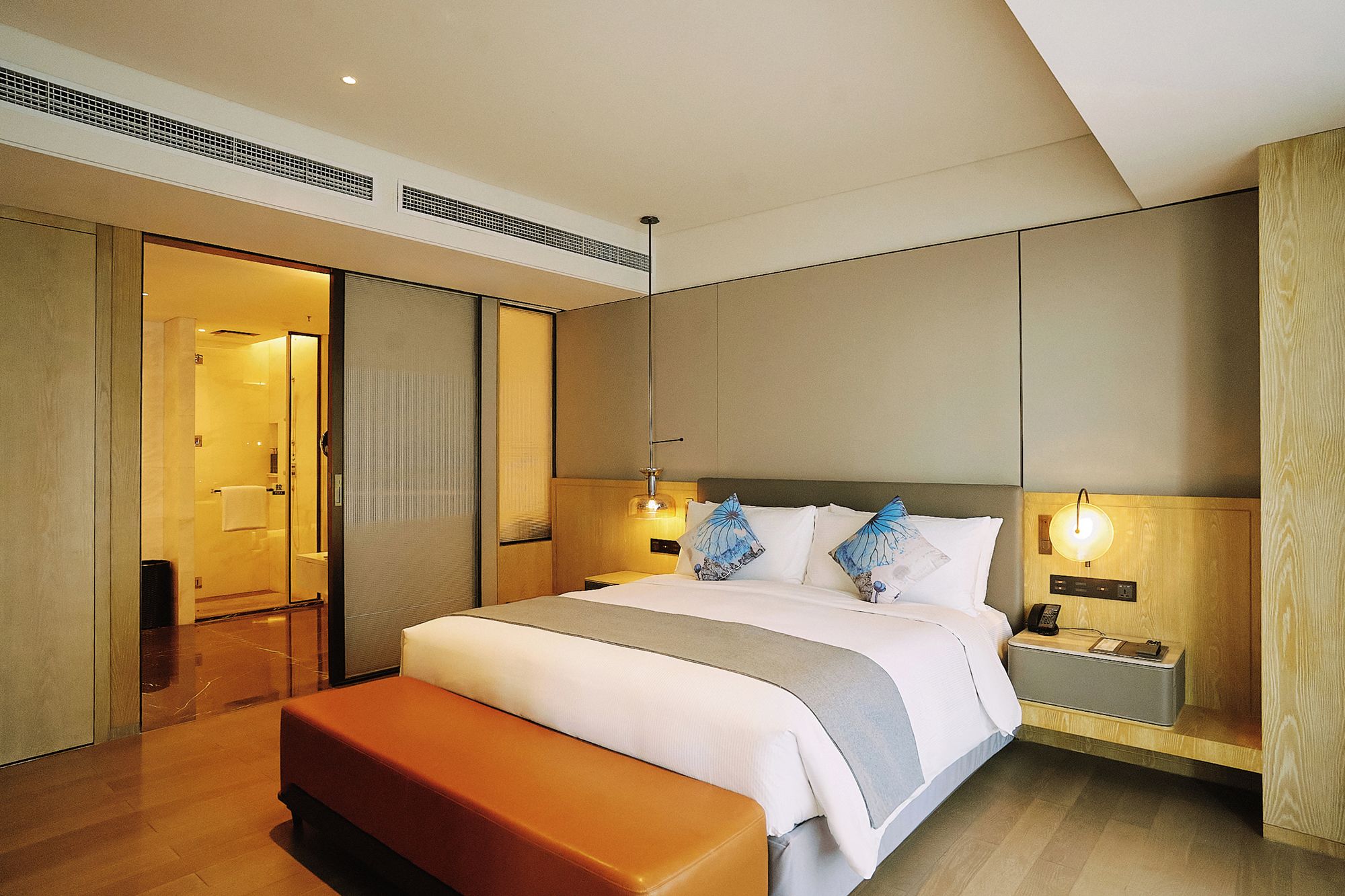 Una habitación de hotel con una cama, mesitas de noche, un banco y un vestidor.