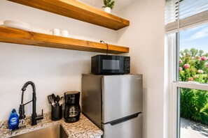 Una cocina con un refrigerador de acero inoxidable, un microondas encima, una cafetera y un lavabo con grifo.