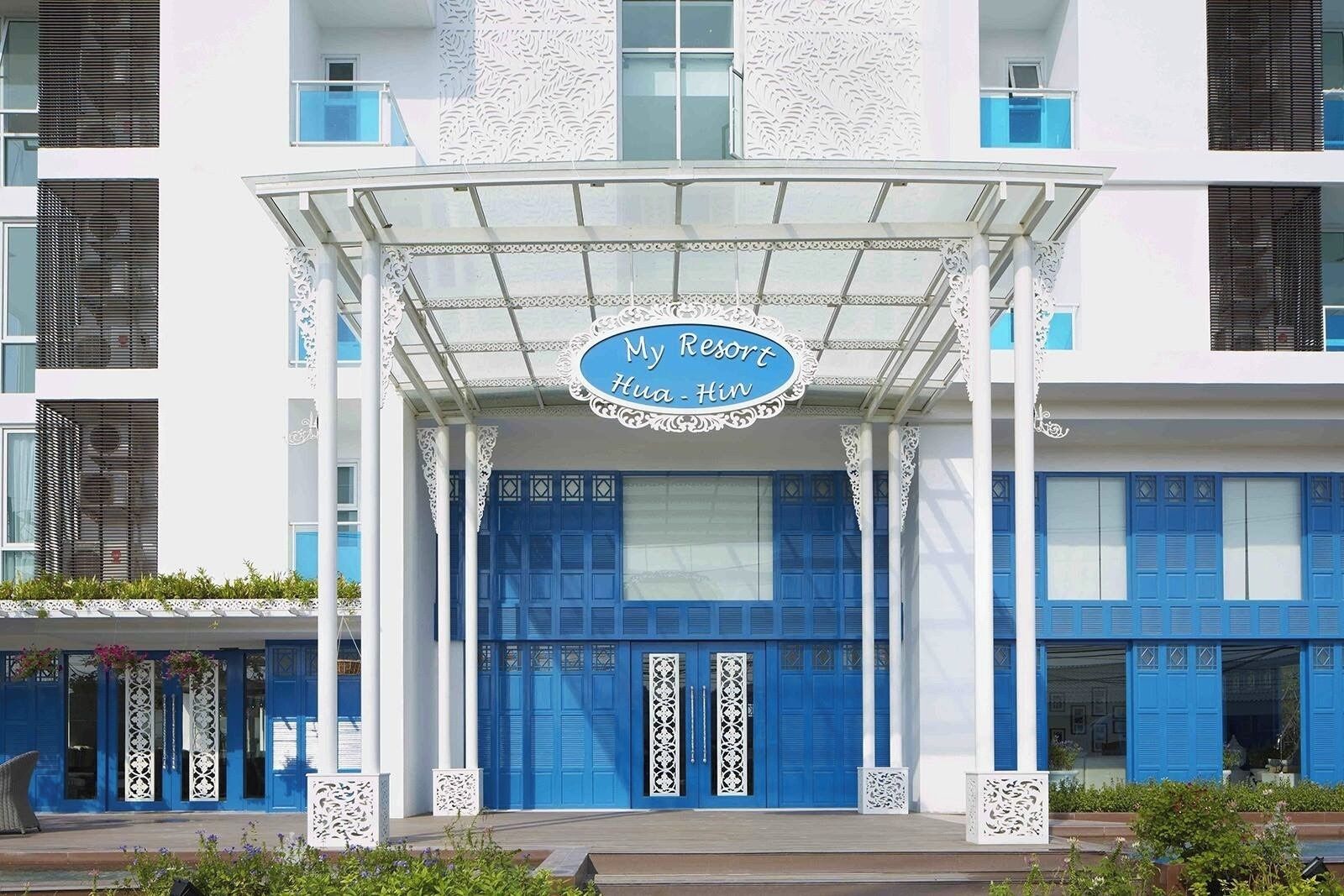 En hotellentrén med en blå fasad, vita kolonner och en skylt med texten ”My Resort Hua-Hin”.