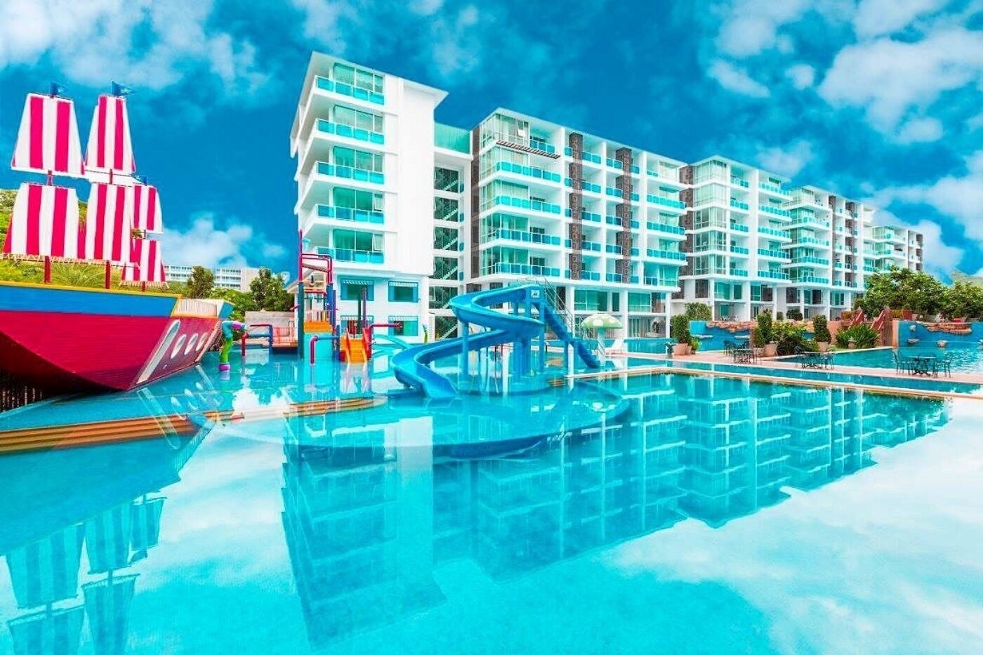 A hotel with a swimming pool, a water slide, and a large building with multiple balconies.