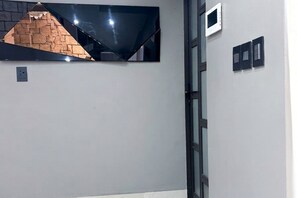 Ein Zimmer mit einem großen Spiegel, der eine Ziegelwand reflektiert, einer Tür mit Fensterteil und einem Lichtschalter an der Wand.