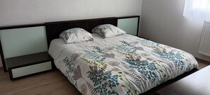 Un lit avec une couvre-lit à motifs floraux, deux oreillers, une table de chevet et une petite table d’appoint.