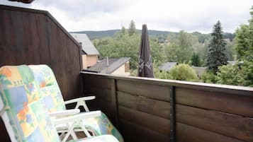 A balcony with a wooden railing, a colorful chair, and a view of a residential area with trees and houses.