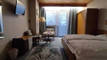 Ein Hotelzimmer mit einem Bett, einem Schreibtisch, einem Stuhl, einem Fernseher und einem Fenster mit Vorhängen.