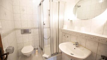 Ein Badezimmer mit einer Duschkabine, einer Toilette und einem Waschbecken mit Spiegel.