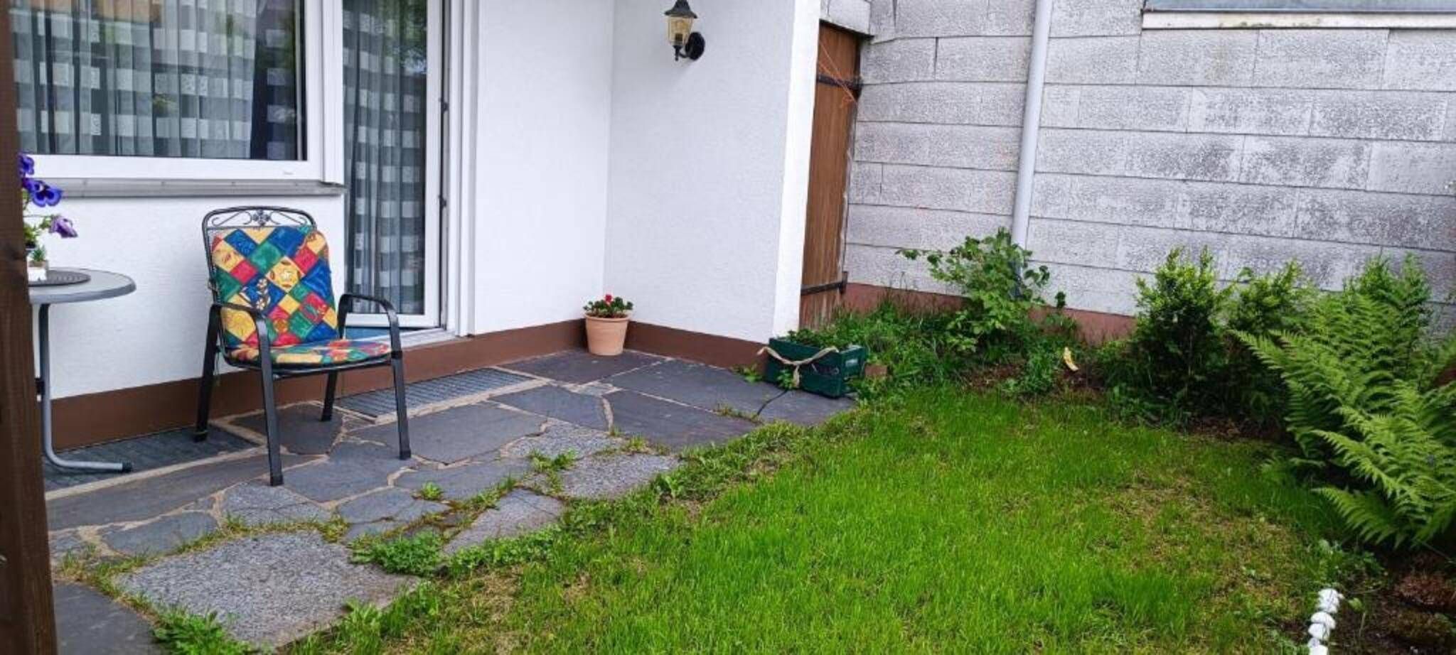 Eine Terrasse mit einem Stuhl, einer Topfpflanze und einem Steinweg, der zu einem Haus führt.