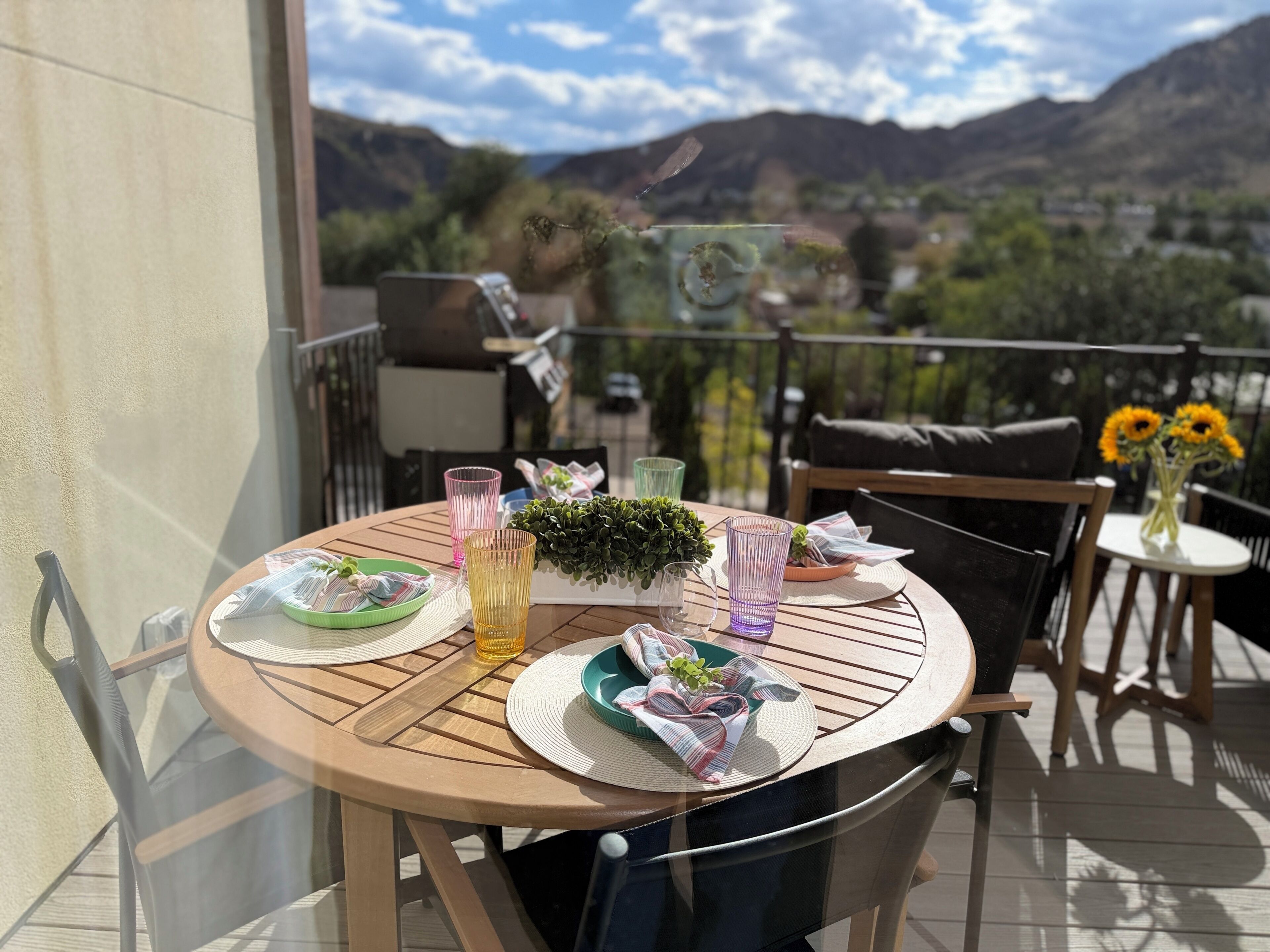 Une table ronde avec des assiettes, des verres et une petite plante, sur un balcon offrant une vue sur les montagnes.