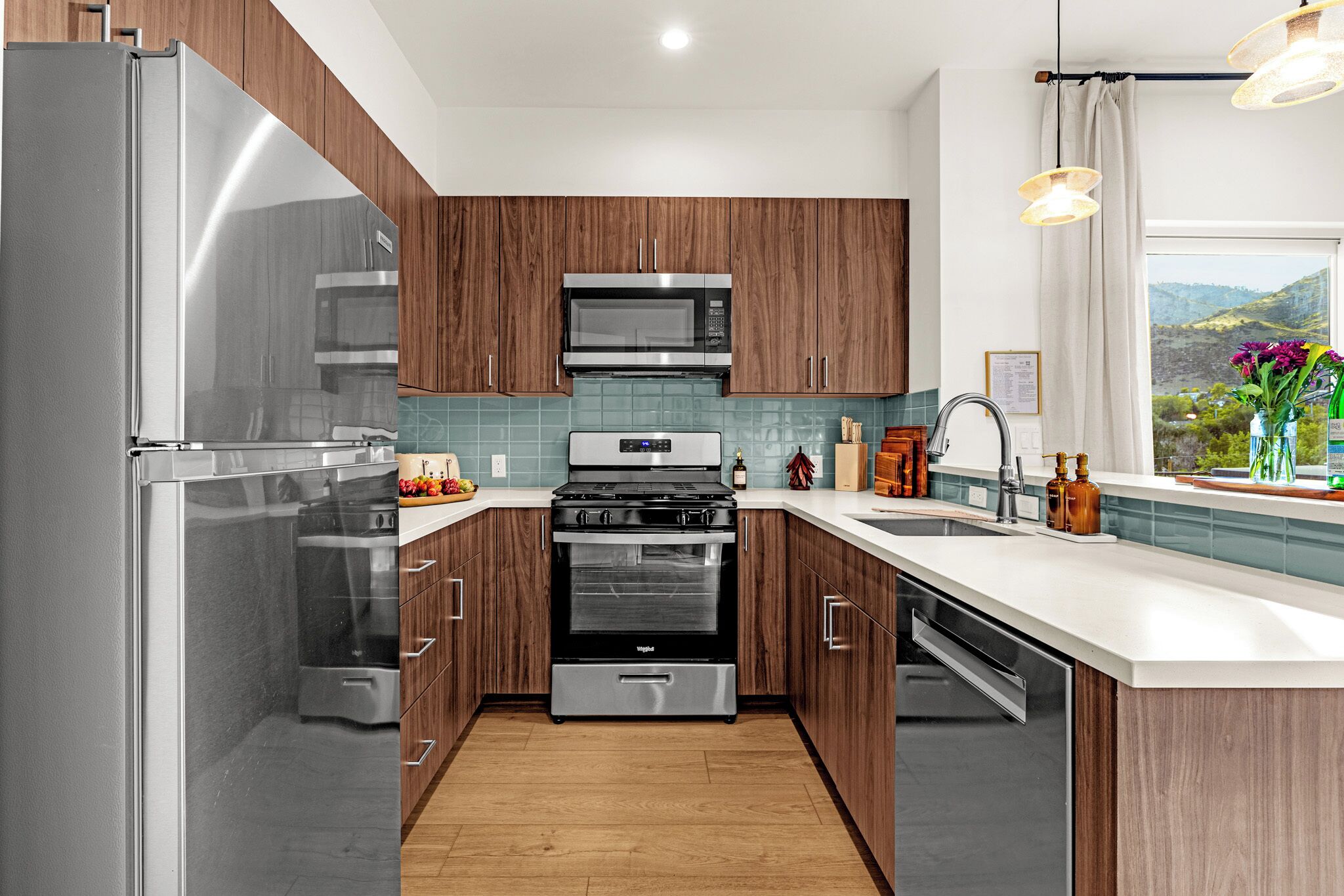 A modern kitchen with stainless steel appliances, wooden cabinets, and a view of the outdoors.