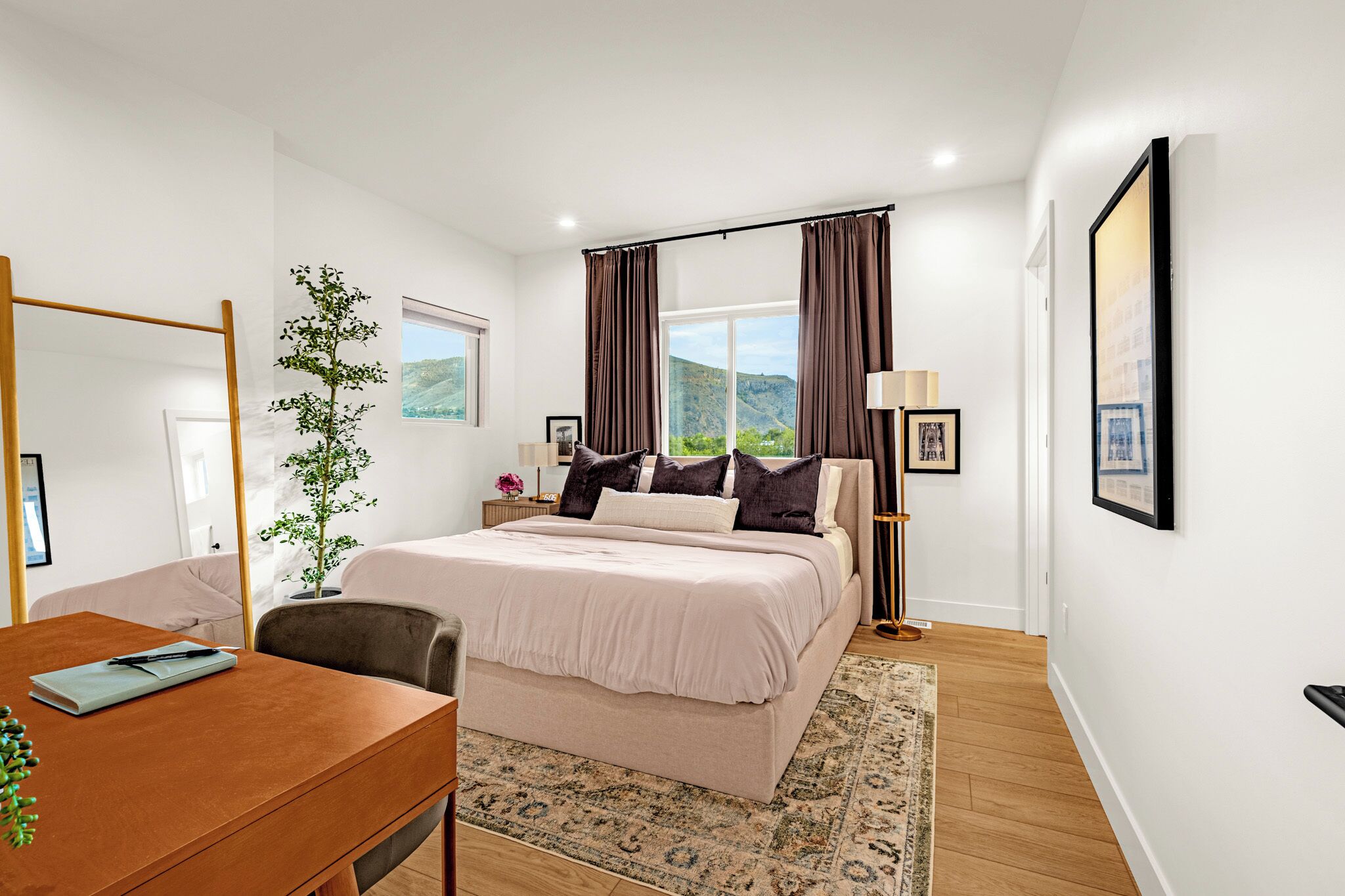 Quarto com cama, escrivaninha, cadeira, planta, janela com cortinas e vista para o exterior.