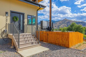 Un edificio moderno con un recinto in legno, una scala che conduce a una porta e una vista sulle montagne sullo sfondo.