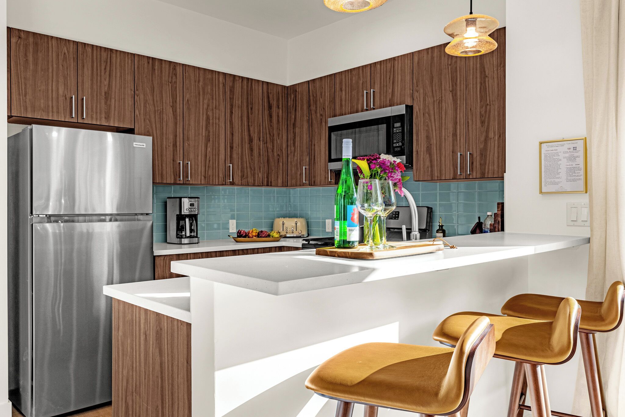 Une cuisine moderne avec des meubles en bois, un réfrigérateur en acier inoxydable, une machine à café, un grille-pain et un coin bar avec des tabourets.